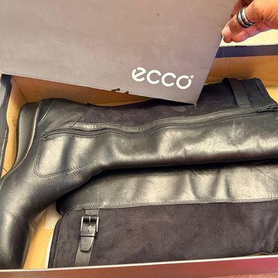 Pair of women's Ecco black leather and suede tall boots, featuring side zippers and buckle details, displayed in their original shoe...