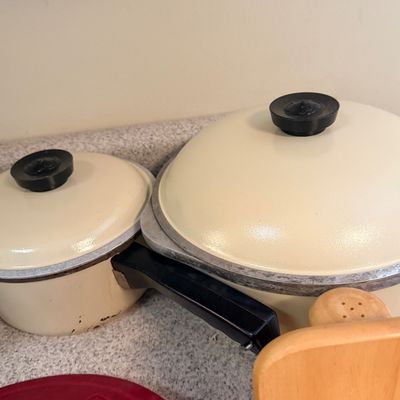 Vintage off-white enamel pots with black handles and lids, showing light wear.