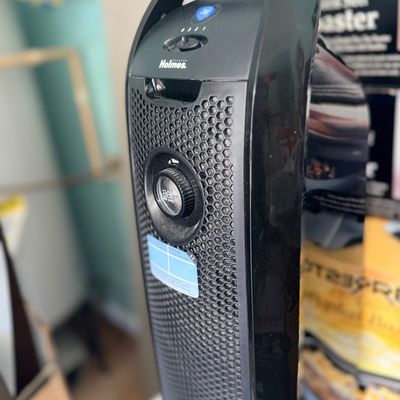 Black Holmes tower air purifier featuring a honeycomb front grille, built-in carrying handle, and top control dial.