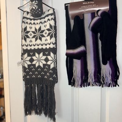 Two cold-weather knit sets hanging on a door, including a grey and white Nordic snowflake patterned scarf with matching socks and a...