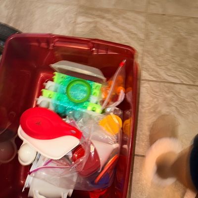 Red plastic storage tote filled with various kitchen organization items, including Tupperware lids, funnels, plastic molds, and small...