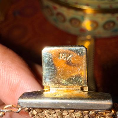 Close-up of a gold mesh bracelet clasp stamped with an 18K purity hallmark.