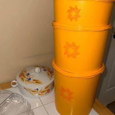 Set of three vintage yellow Tupperware nesting canisters with sunburst floral motifs, displayed alongside a covered ceramic casserole dish.
