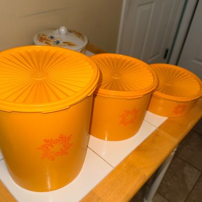 Set of three vintage yellow-orange Tupperware Servalier canisters with starburst lids, circa 1970s.