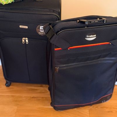 Two black soft-sided rolling suitcases, including an American Tourister model and a Trident model, shown on a hardwood floor.