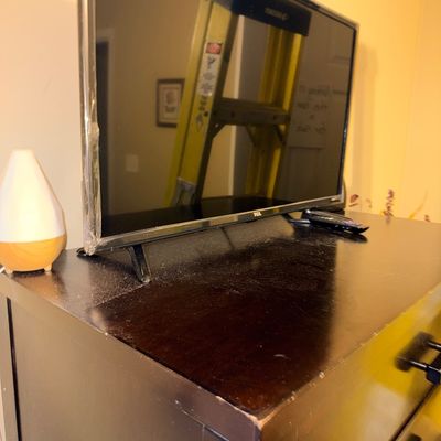 Modern TCL flat-screen television resting on a dark wood dresser alongside a small essential oil diffuser.