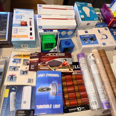 Assortment of household items, including GE light bulbs, Duracell batteries, lens wipes, digital alarm clocks, and fitness accessories,...