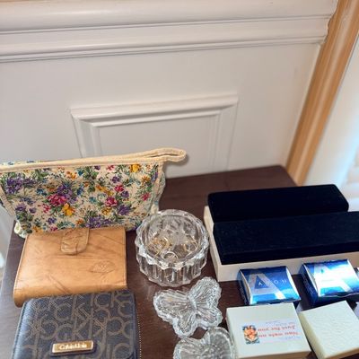 Assortment of vanity items including a Calvin Klein monogram wallet, a tan leather wallet, a floral makeup bag, crystal trinket dishes,...
