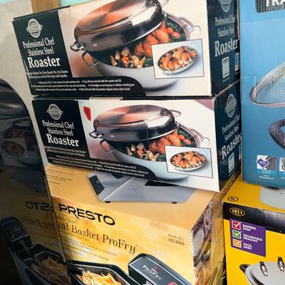 Stack of boxed kitchen appliances including two Gourmet Standard Professional Chef stainless steel roasters and a Presto Dual Basket...