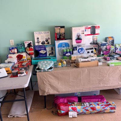 Assorted modern household items, small appliances, and electronics, mostly boxed, displayed on folding tables.