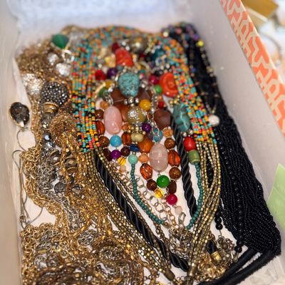 Shoebox filled with an assortment of vintage costume jewelry, including multi-strand seed bead necklaces, gold-tone chain necklaces, and...
