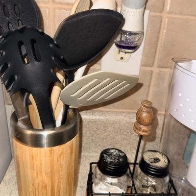 Countertop collection featuring a bamboo utensil crock filled with assorted kitchen tools alongside a salt and pepper shaker set in a...