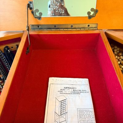Open light wood standing jewelry armoire featuring a top compartment lined with red felt, an inset mirror, and the original instruction...