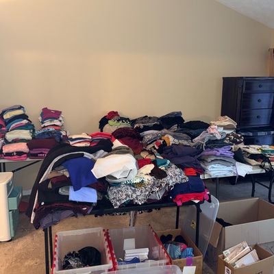 Large collection of folded women's clothing arranged on folding tables, accompanied by plastic storage bins and cardboard boxes...