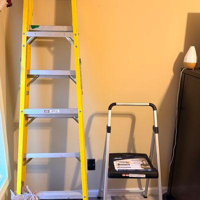 Six-foot yellow fiberglass A-frame stepladder alongside a smaller two-step aluminum folding step stool with a black plastic top step.