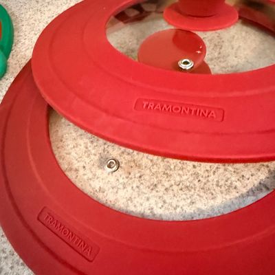 Pair of modern Tramontina universal cookware lids featuring red silicone rims and tempered glass centers with steam vents.