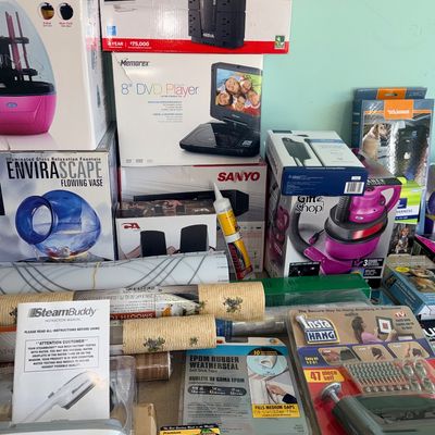 Collection of boxed household items and electronics, including a CyberPower battery backup unit, a Memorex portable DVD player, an...