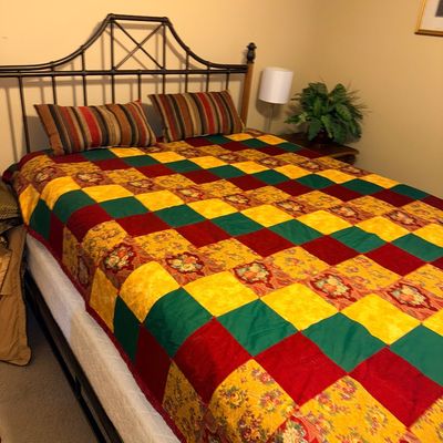 Wrought iron queen bed frame featuring a geometric spindle headboard, dressed in a colorful patchwork quilt and striped accent pillows.
