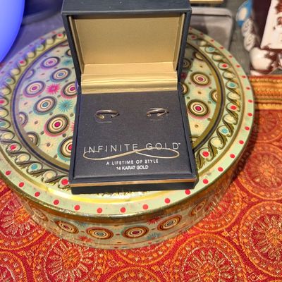Pair of Infinite Gold 14-karat gold hoop earrings in original black display box, set atop a decorative patterned tin.