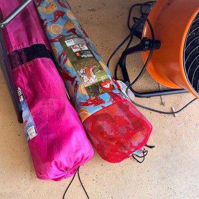 Pair of portable folding camp chairs in carrying bags, including an Ozark Trail crawfish print chair and a bright pink Academy Sports chair.