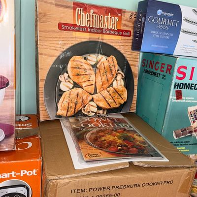 Boxed Chefmaster Smokeless Indoor Barbeque Grill resting on a Power Pressure Cooker Pro shipping box, flanked by other small appliances.