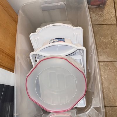 Large clear plastic storage tote filled with assorted household items and food storage containers.