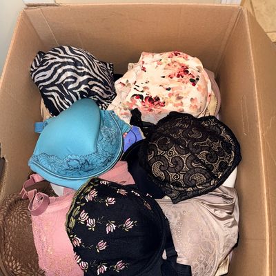 Cardboard box filled with an assortment of women's bras featuring various colors, patterns, and lace details.