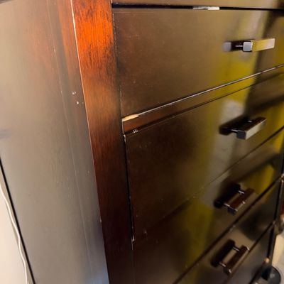 Contemporary dark espresso wooden chest of drawers featuring linear metal pulls and minor wear along the edges.