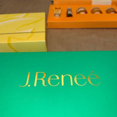 Bright green J. Reneé shoe box featuring gold metallic lettering, alongside other boxed cosmetic and beauty gift sets.