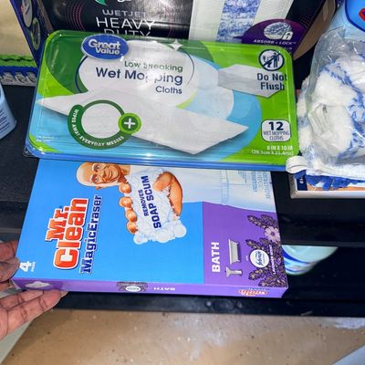 Assortment of household cleaning supplies, including Mr. Clean Magic Eraser Bath pads, Great Value wet mopping cloths, and Swiffer WetJet...