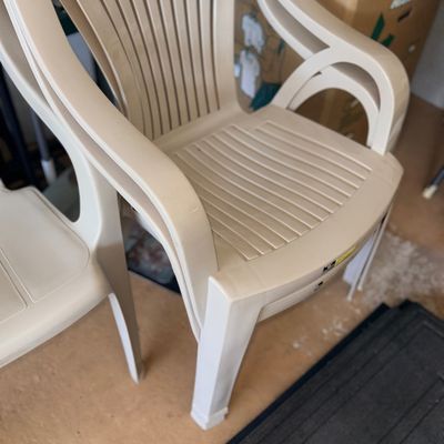 Stacked beige plastic resin outdoor patio lawn chairs with high slatted backs and armrests.