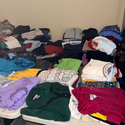 Large assortment of folded vintage and modern clothing arranged on folding tables, including graphic tees, fleece pullovers, and jackets.