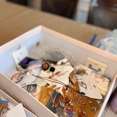White shoe box filled with various pieces of costume jewelry, including beaded necklaces, drop earrings, and branded Monet display cards.