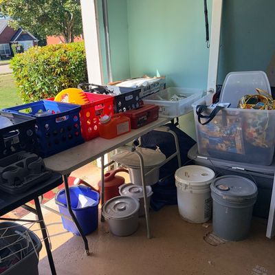 Assorted household items, plastic crates, storage bins, and 5-gallon buckets set up in a garage for an estate sale.