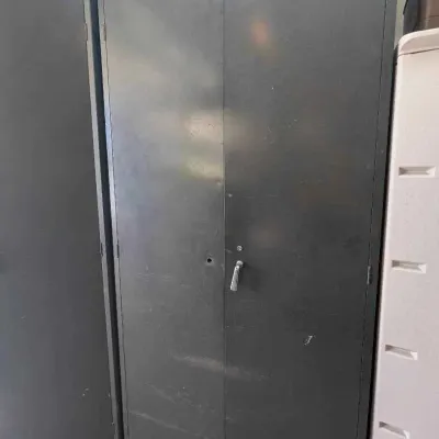 Sale Photo Thumbnail #135: Vintage industrial metal storage cabinet with double doors and a locking handle, showing some wear from age and use.