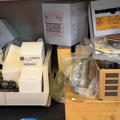 Sale Photo Thumbnail #114: Snap-on cordless impact wrench alongside various boxed hardware, Lawson parts, and Brother P-Touch TZ-tape cassettes on a shelf.