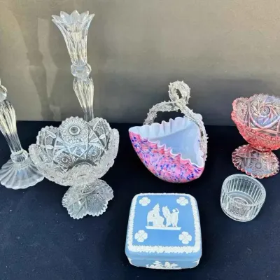 Sale Photo Thumbnail #154: Assorted vintage glassware and collectibles, including a pair of tall clear glass candlesticks, a clear cut-glass compote, a pink and blue spatter glass basket with a clear handle, a pink cut-glass compote, a small ribbed glass dish, and a blue Wedgwood j