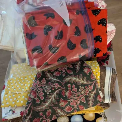 Sale Photo Thumbnail #169: Assorted quilting fabric remnants and fat quarters in various patterns, including floral, polka dot, and novelty prints, stored in a plastic bin.