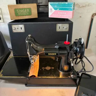 Sale Photo Thumbnail #174: Vintage Singer Featherweight 221 sewing machine with its original black carrying case, foot pedal, and boxed buttonhole and automatic zigzagger attachments.