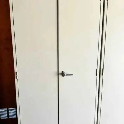 Sale Photo Thumbnail #51: Tall, industrial-style metal storage cabinet in a light gray finish, featuring double doors with a central locking handle.