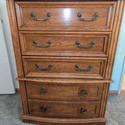 Sale Photo Thumbnail #91: Vintage oak tallboy dresser featuring five drawers with decorative brass hardware and a slightly bowed lower section.