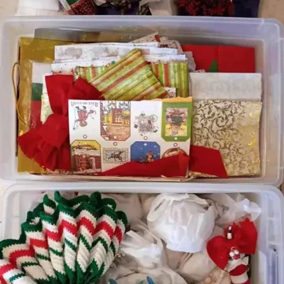 Sale Photo Thumbnail #180: Assorted Christmas decorations and gift wrapping supplies, including gift tags, ribbons, tissue paper, and crocheted items, organized in plastic storage bins.