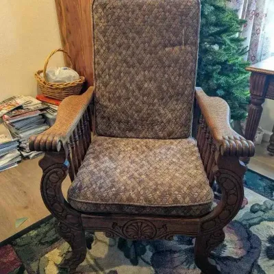 Sale Photo Thumbnail #17: Antique carved oak Morris-style armchair featuring ornate scrollwork on the legs and arm supports, fitted with patterned brown fabric cushions.