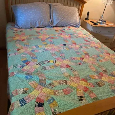 Sale Photo Thumbnail #16: Vintage double wedding ring quilt with a mint green background and colorful patterned rings, displayed on a wooden bed frame.