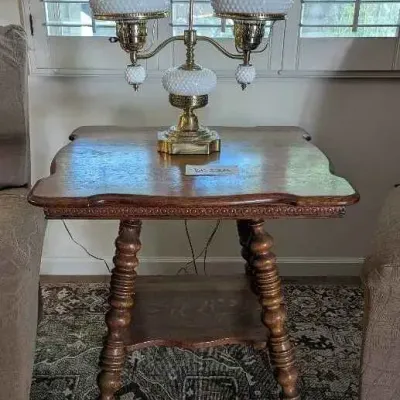 Sale Photo Thumbnail #146: Vintage Fenton hobnail milk glass double student lamp with brass base, displayed on a wooden side table with turned legs.