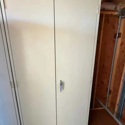 Sale Photo Thumbnail #40: Tall beige metal storage cabinet with double doors and a central locking handle, suitable for garage or utility use.
