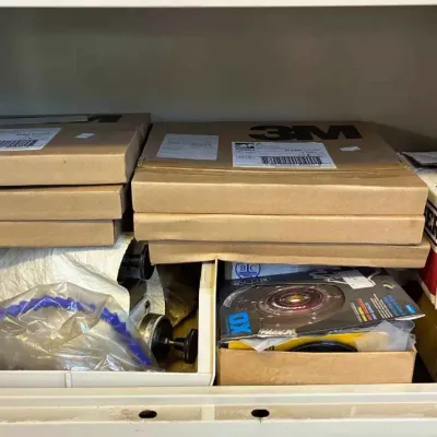 Sale Photo Thumbnail #118: A shelf containing various boxed items, including 3M products and a Grainger box, alongside plastic bins with tools and accessories.