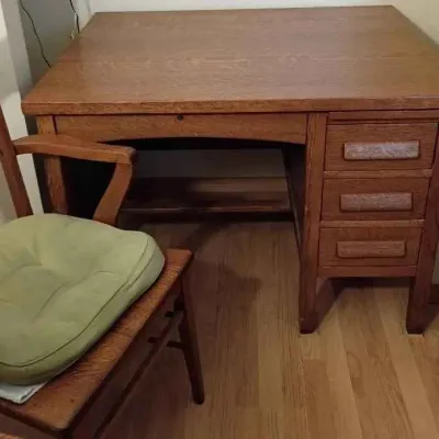Sale Photo Thumbnail #84: Vintage Mission-style oak desk featuring three side drawers with wooden pulls, paired with a matching wooden armchair with a green seat cushion.