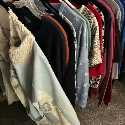 Sale Photo Thumbnail #97: Assorted women's tops and sweaters, including a light blue denim and knit jacket, hanging on a clothing rack.