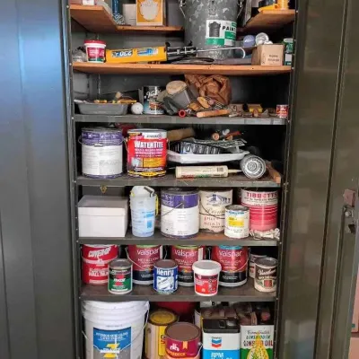 Sale Photo Thumbnail #44: Metal storage cabinet filled with various home improvement supplies, including paint cans, primers, wood finishes, and painting tools.